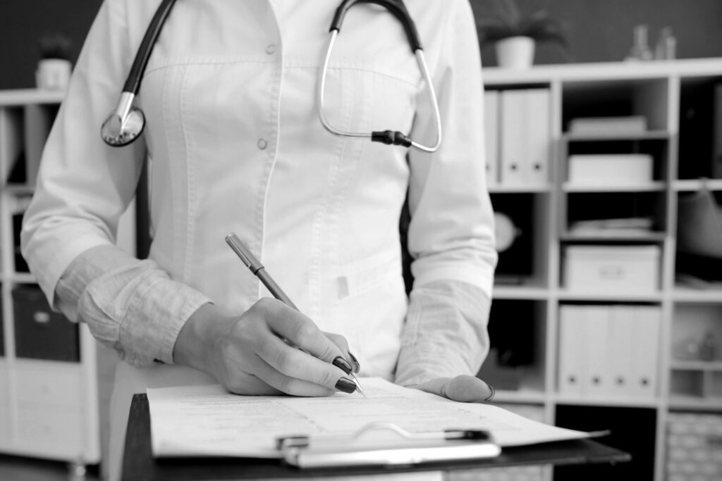 Médica de jaleco preenchendo um documento em uma prancheta no consultório