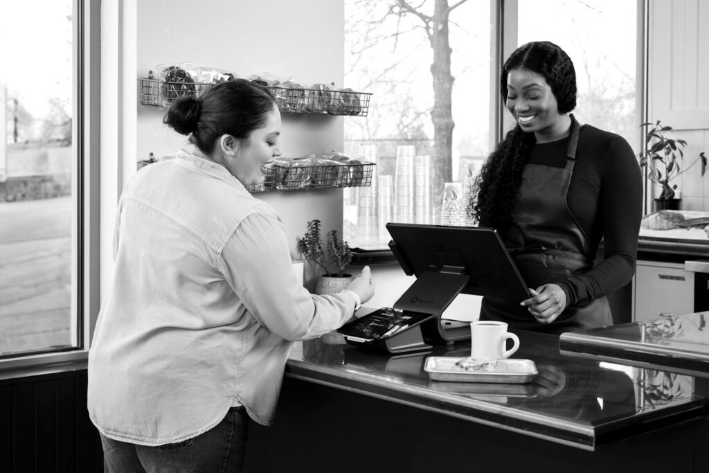 Atendente de avental no balcão de um café registrando a compra de uma cliente